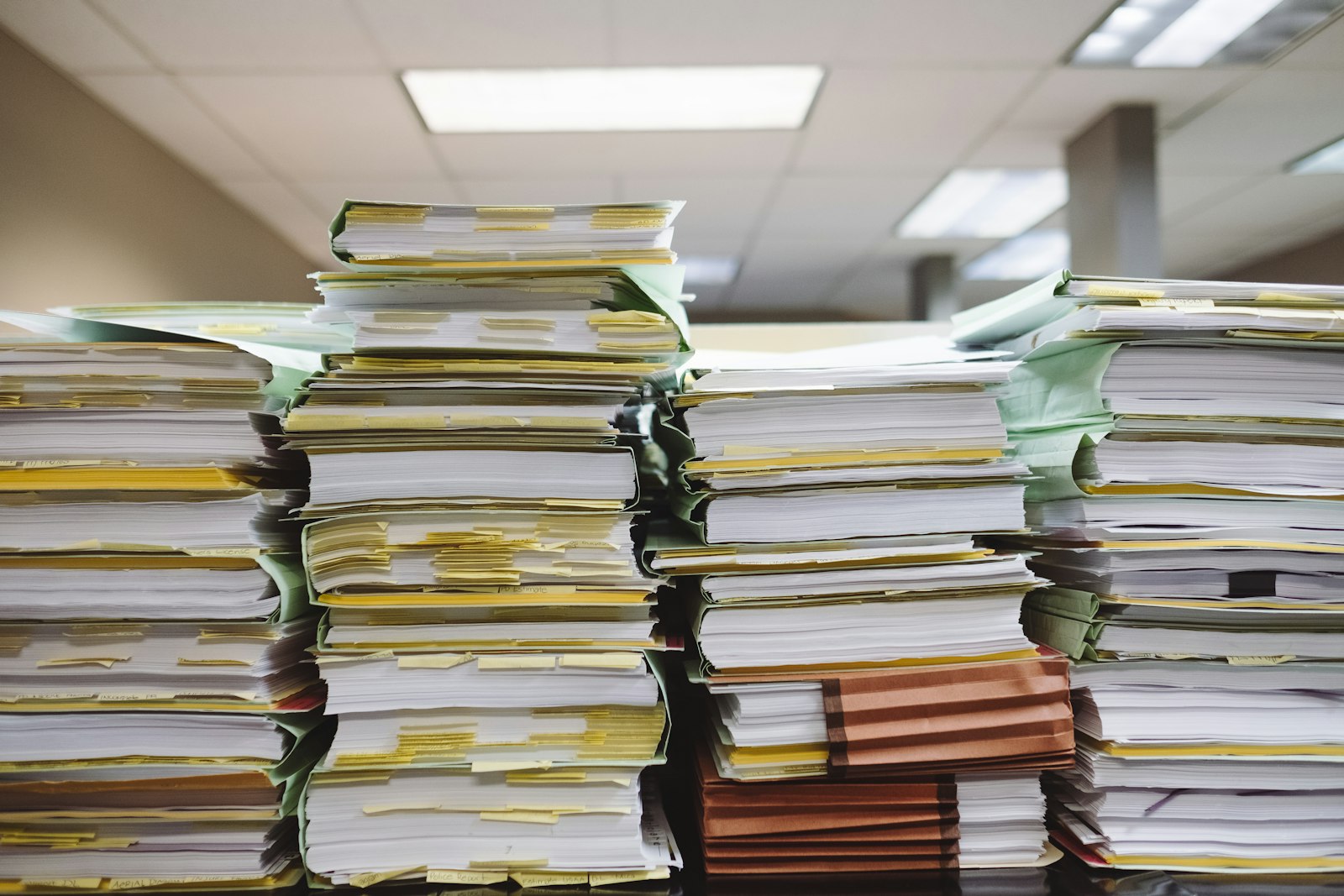 Wysokie stosy papierowych teczek i dokumentów na biurku w biurze — obraz nieuporządkowanej obsługi reklamacji
